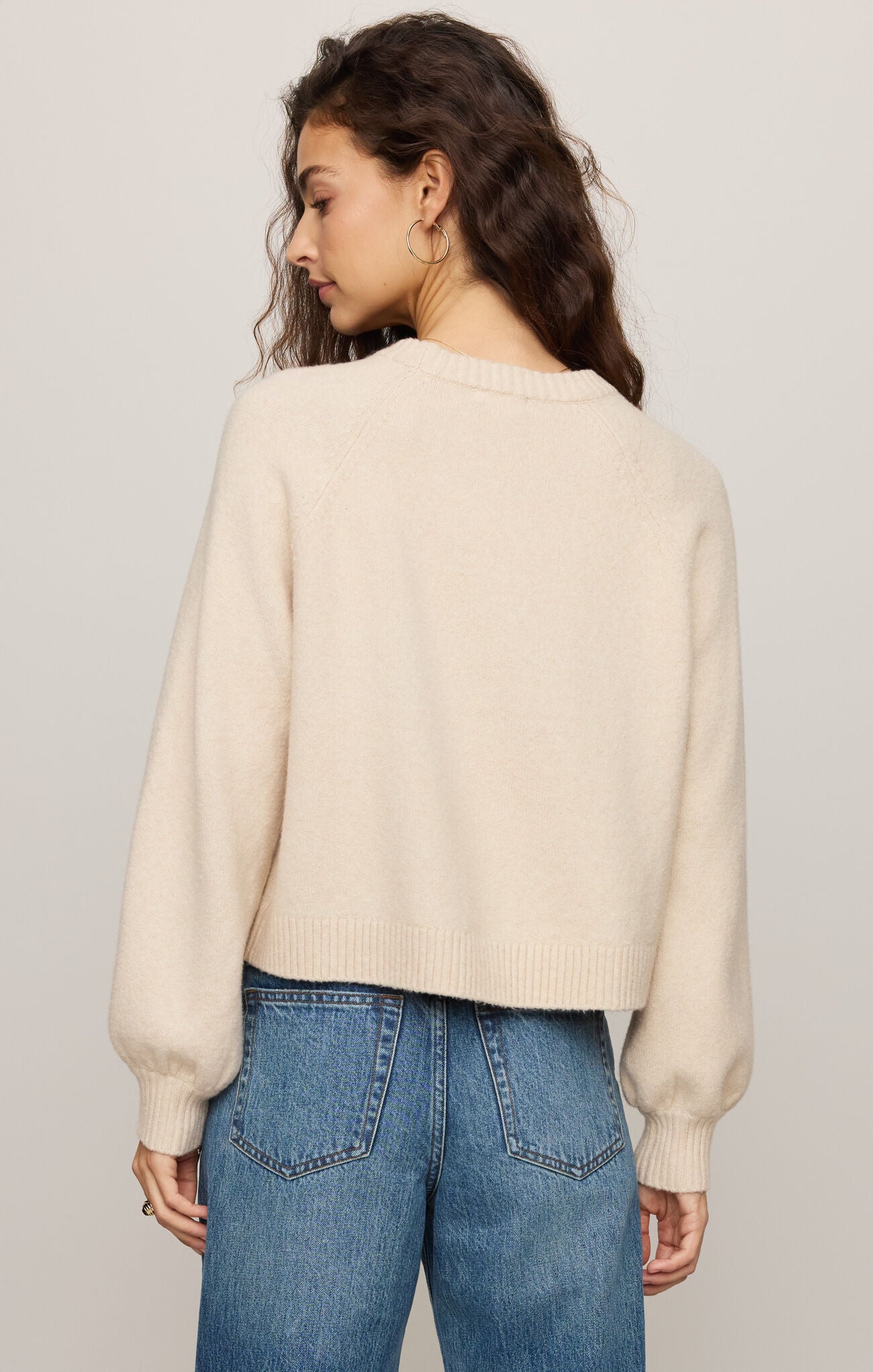 Woman wearing a beige sweater and blue jeans against a plain background