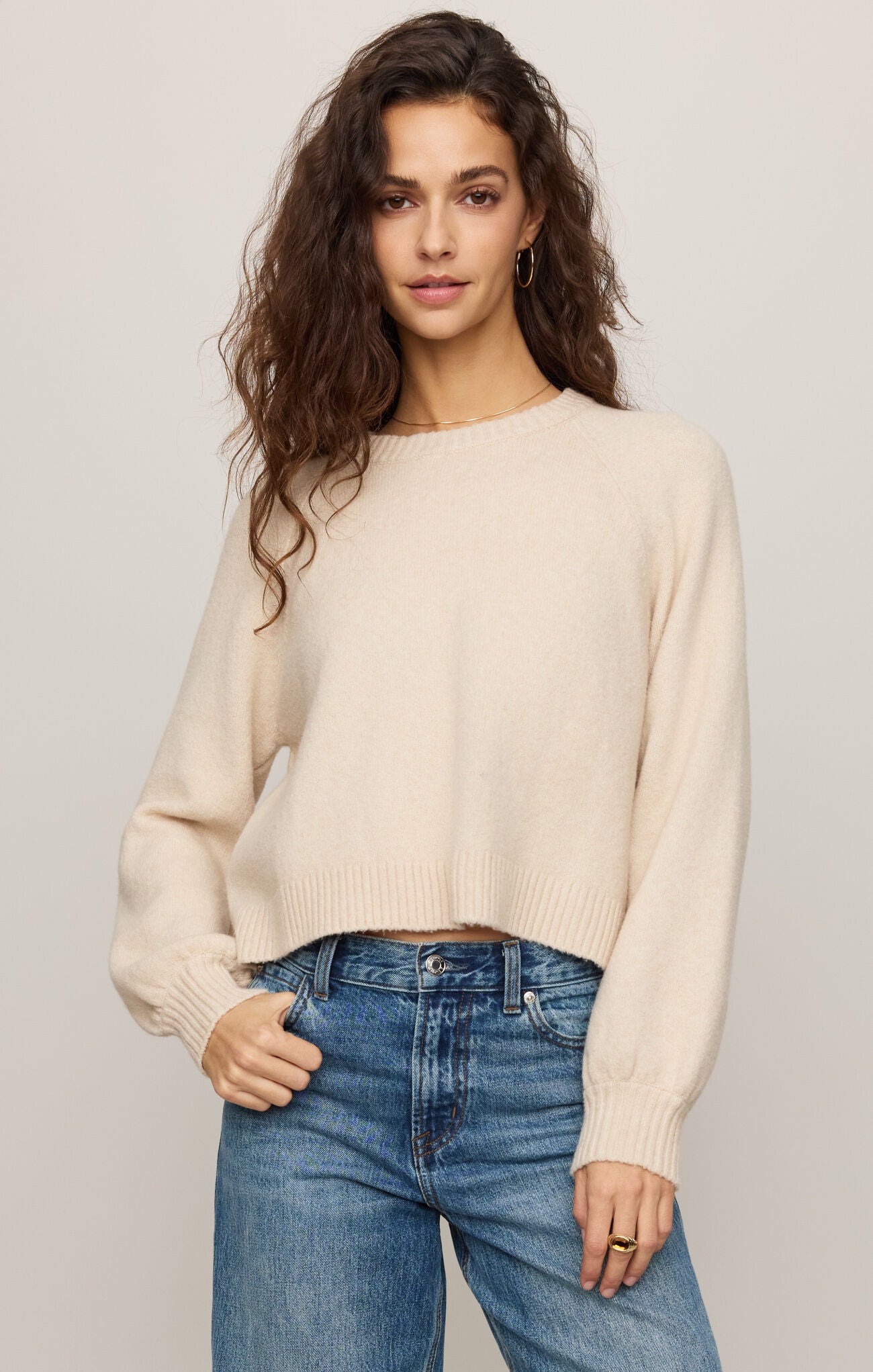 Woman wearing a beige sweater and blue jeans against a plain background