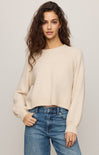 Woman wearing a beige sweater and blue jeans against a plain background