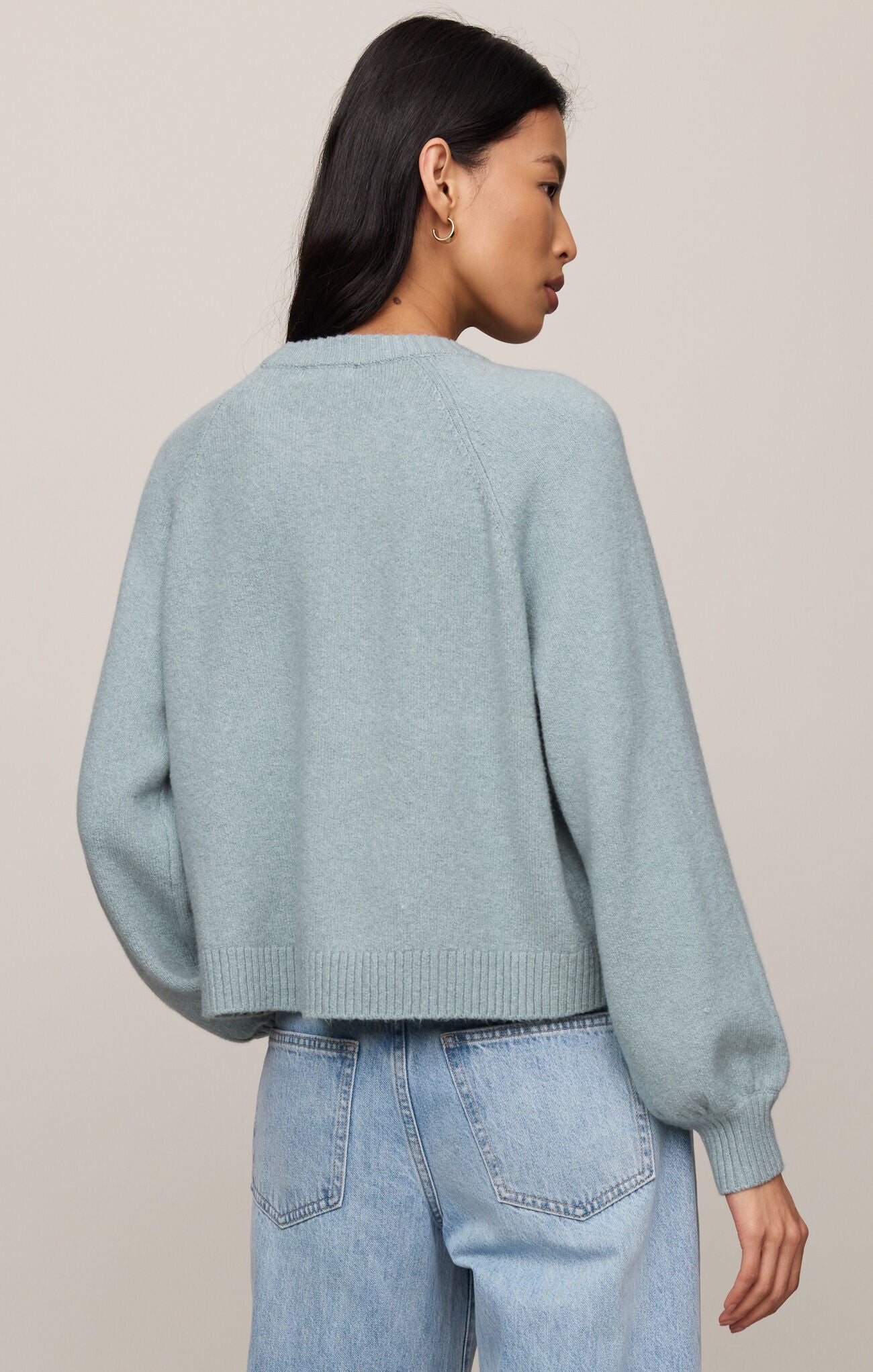 Person wearing a light blue sweater and jeans against a plain background