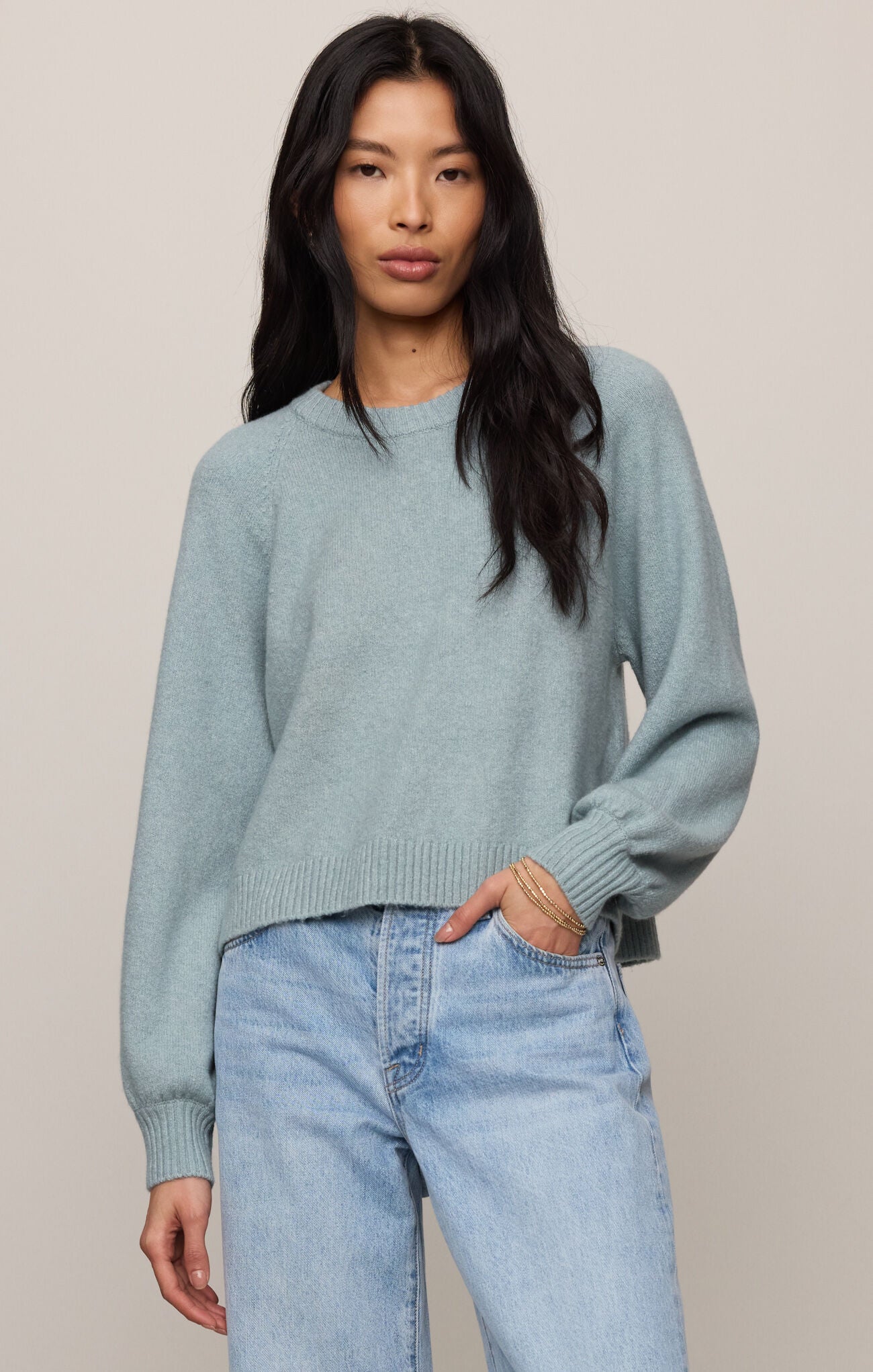 Woman wearing a light blue sweater and jeans against a plain background