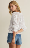 Woman wearing a white knit sweater and denim shorts on a plain background