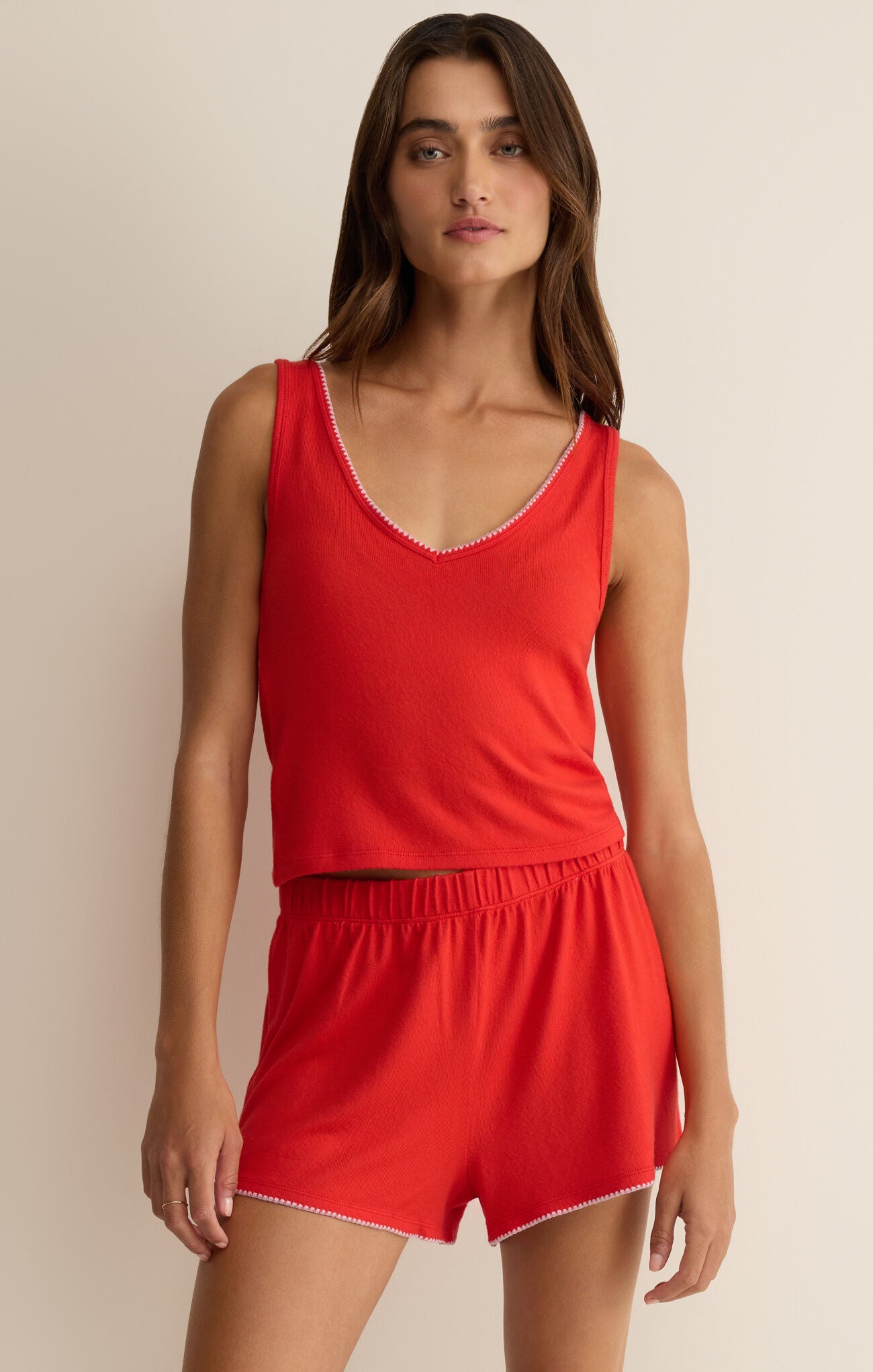 Woman wearing a red tank top and shorts set against a beige background