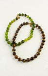 Two beaded necklaces, one green and brown, the other brown and black, on a white background.