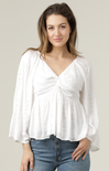 Woman wearing a white blouse with lace details and blue jeans on a plain background