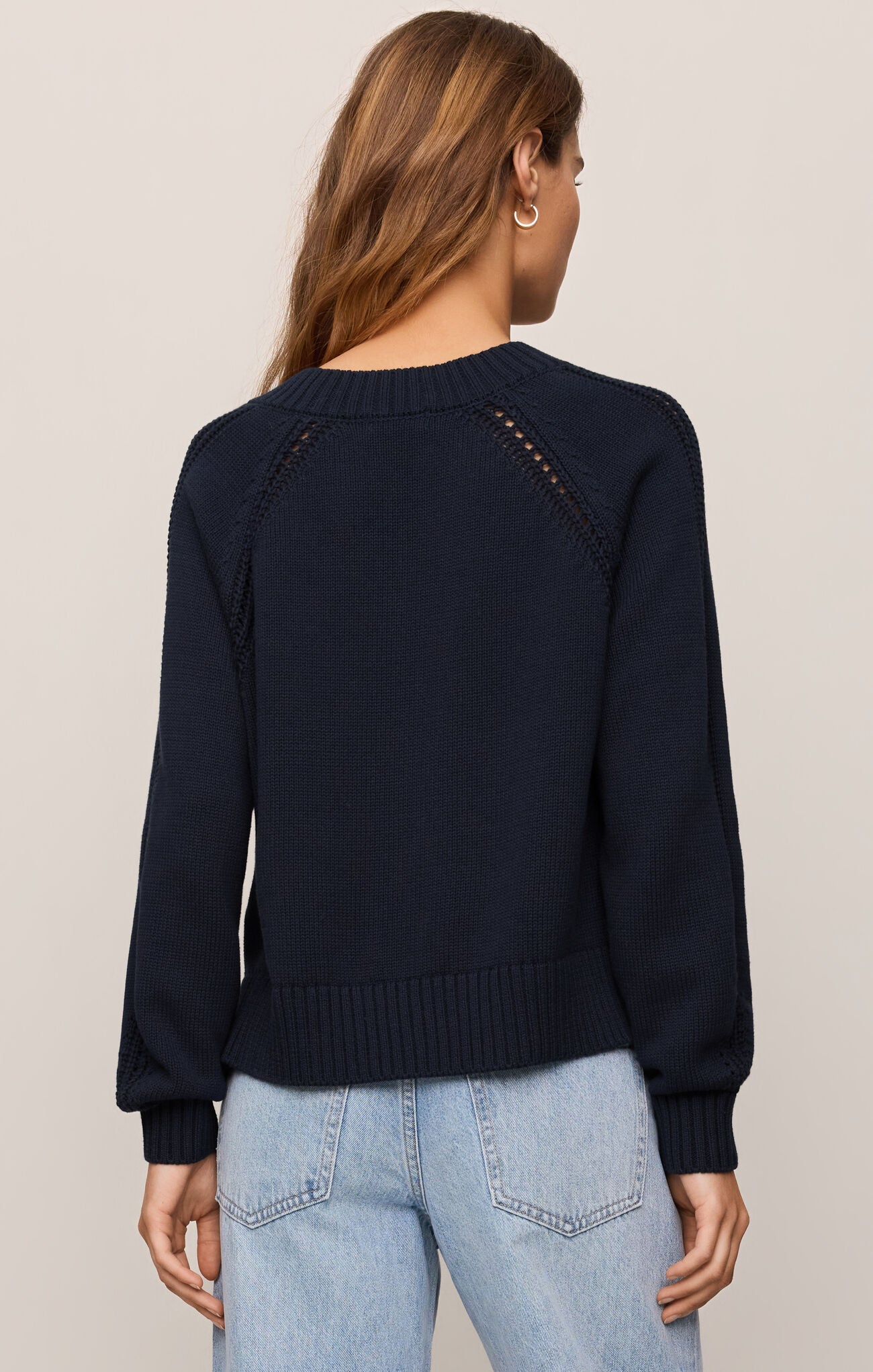 Person wearing a navy sweater with decorative buttons on a plain background