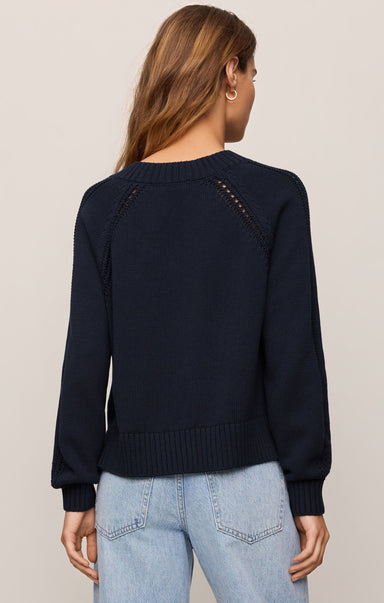 Person wearing a navy sweater with decorative buttons on a plain background