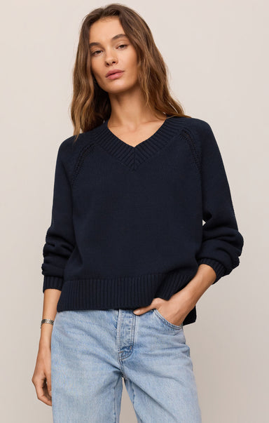 Woman wearing a navy sweater and light blue jeans against a beige background