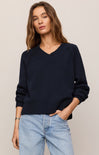 Woman wearing a navy sweater and light blue jeans against a beige background