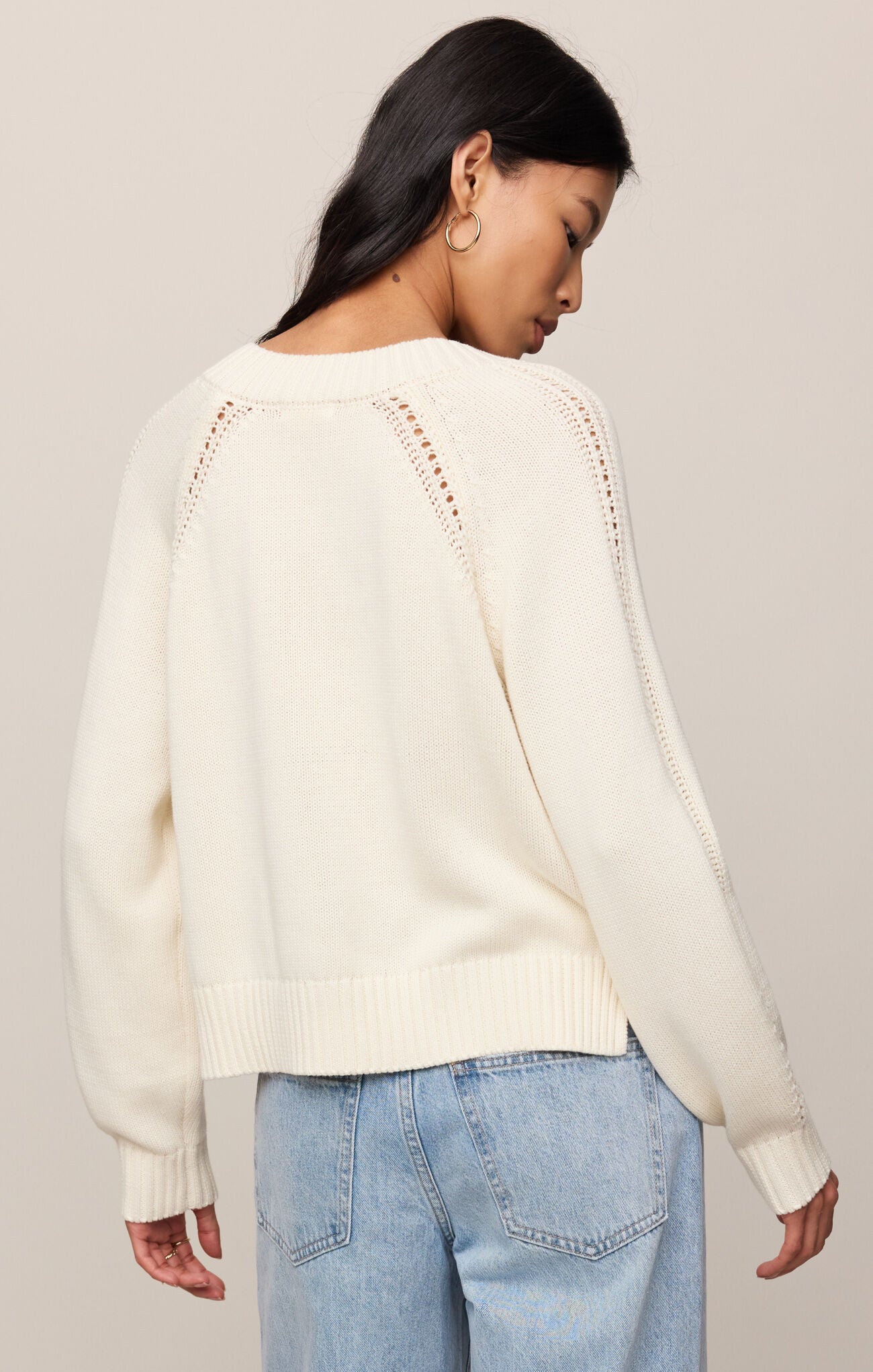 Woman wearing a cream sweater with lace details on a plain background