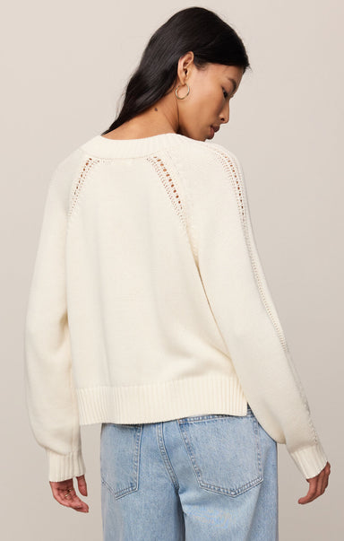 Woman wearing a cream sweater with lace details on a plain background