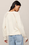 Woman wearing a cream sweater with lace details on a plain background