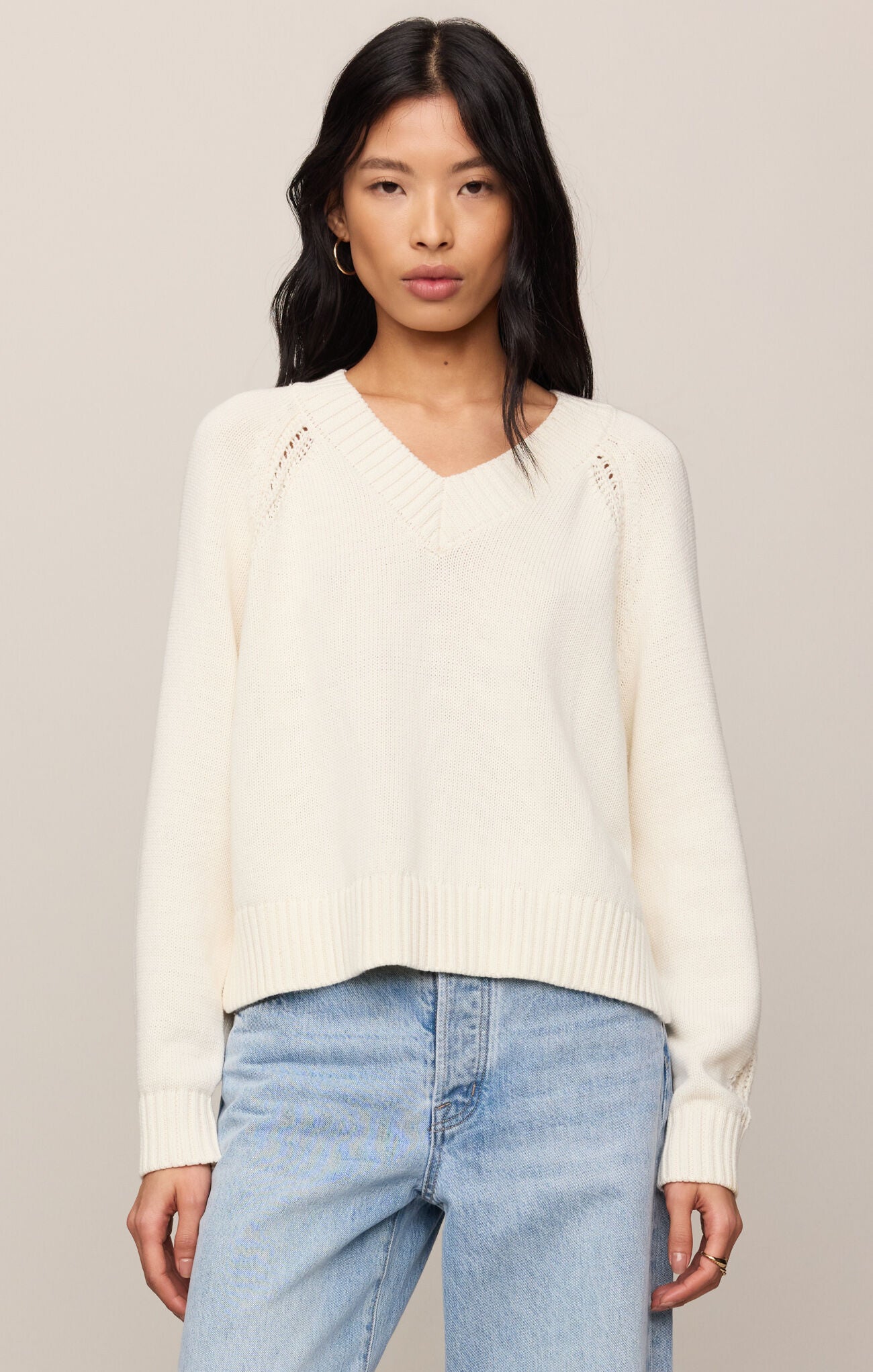Woman wearing a cream sweater and light blue jeans against a neutral background