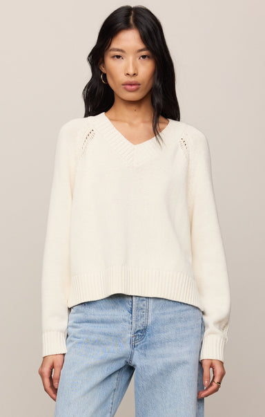 Woman wearing a cream sweater and light blue jeans against a neutral background