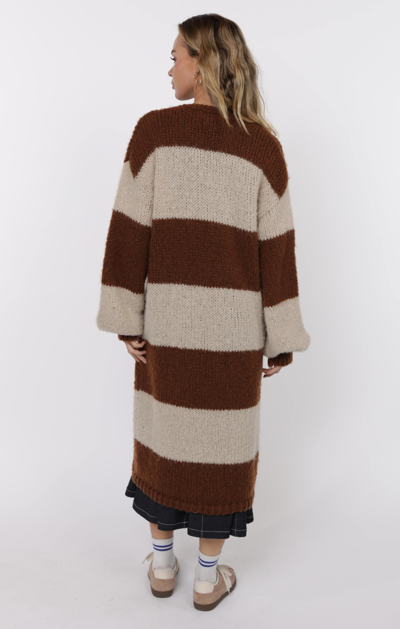 Person wearing a long, striped sweater with brown and beige colors on a white background