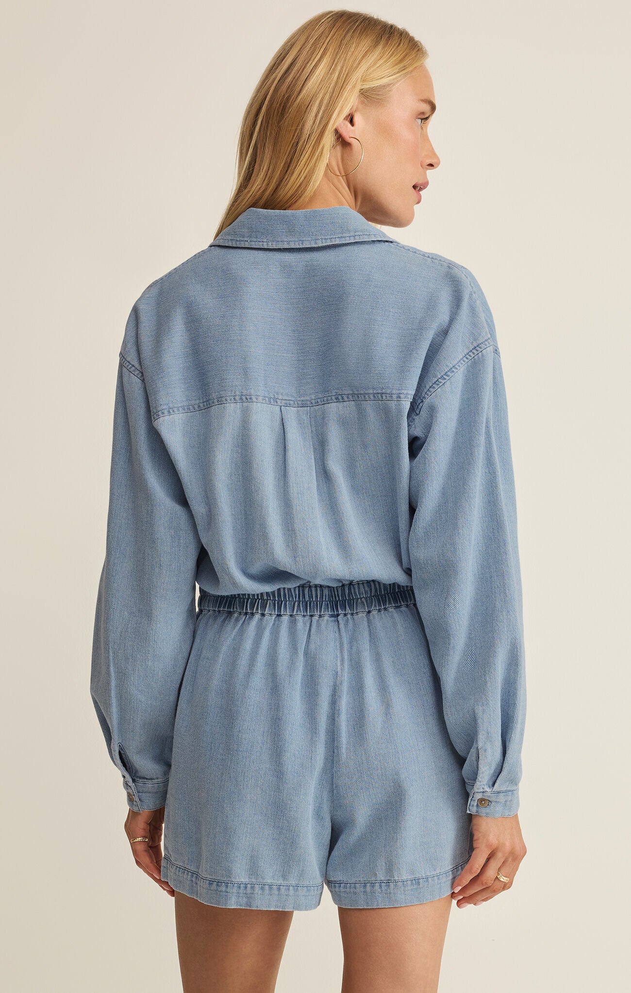Woman wearing a light blue denim romper on a beige background