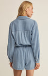 Woman wearing a light blue denim romper on a beige background
