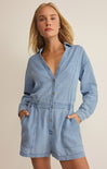 Woman wearing a light blue denim romper against a beige background
