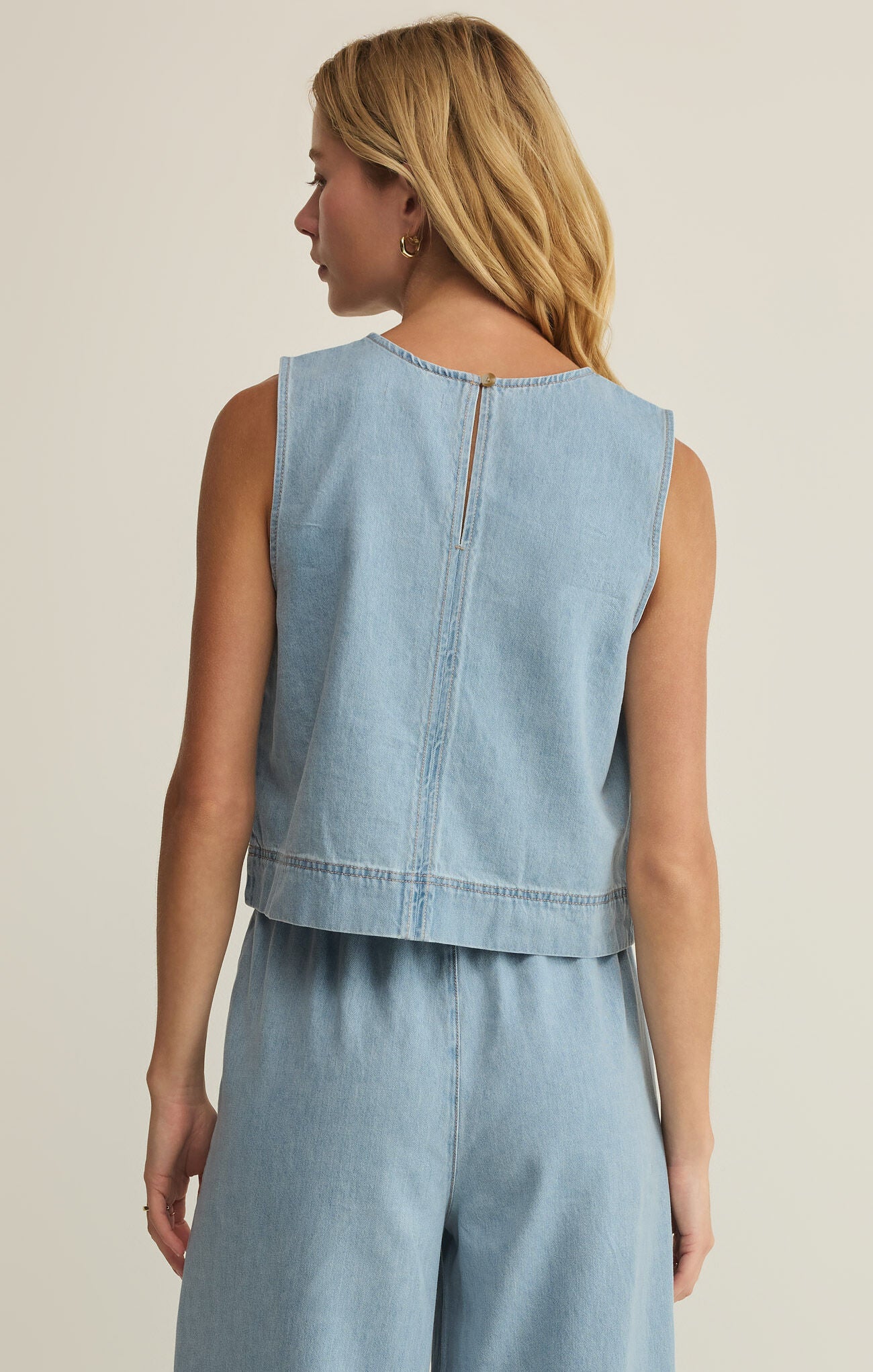 Woman wearing a light blue denim sleeveless top and pants on a beige background