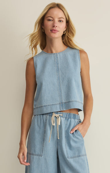 Woman wearing a light blue sleeveless top and wide-leg pants against a beige background