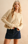 Woman wearing a beige cable knit sweater and denim skirt on a beige background