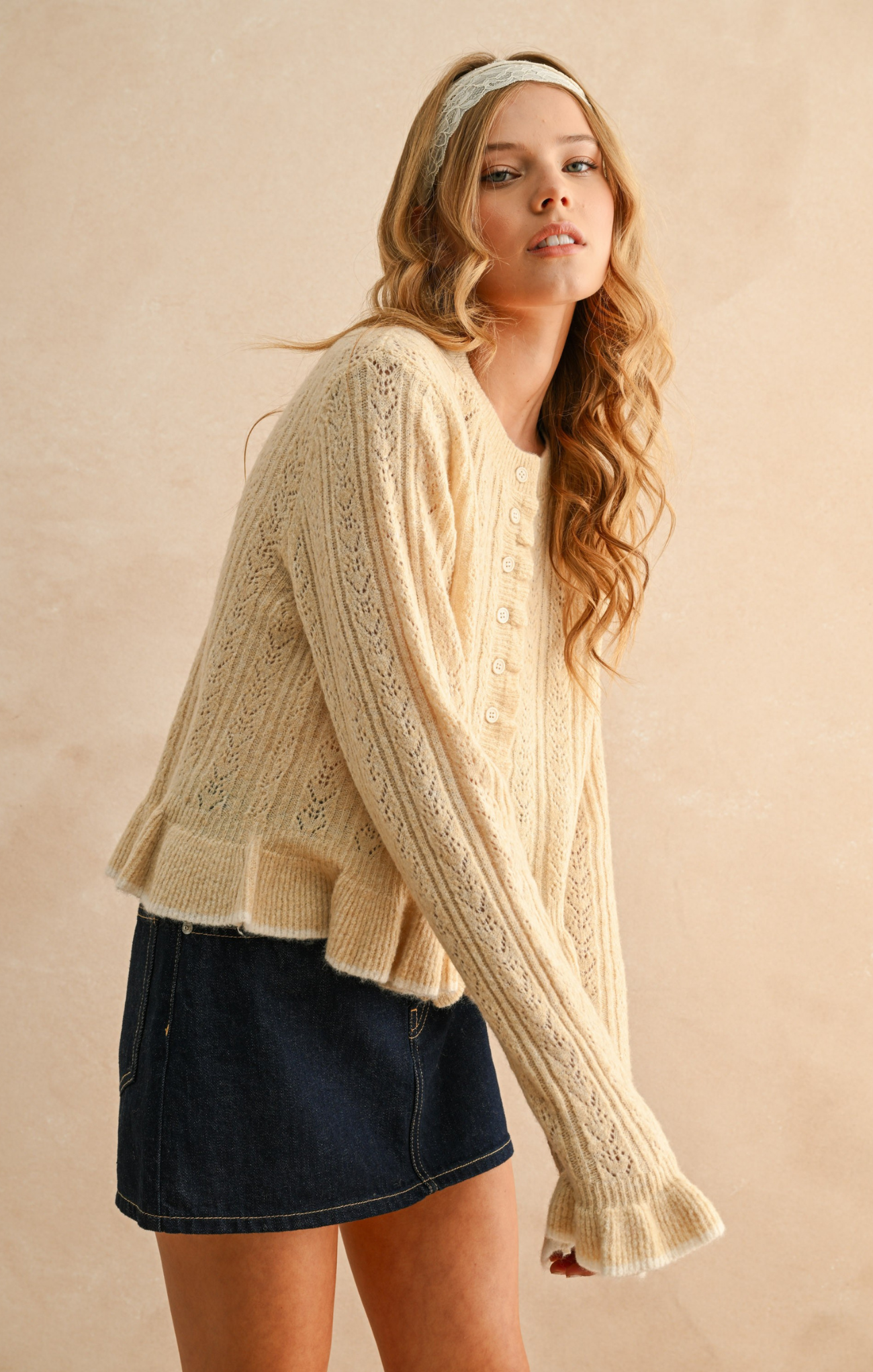 Woman wearing a beige cable knit sweater and denim skirt against a beige background