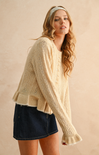 Woman wearing a beige cable knit sweater and denim skirt against a beige background