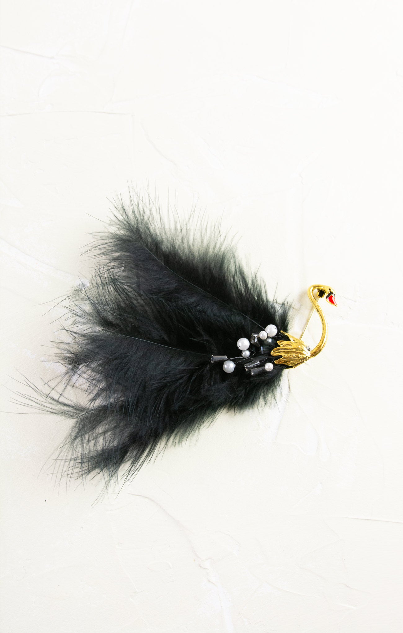 Black feathered hair clip with a gold and yellow swan design on a white background