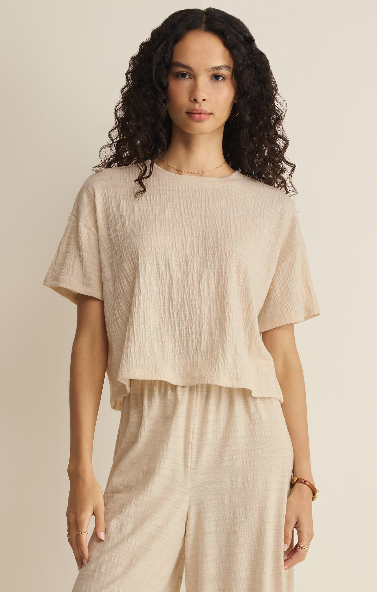 Woman wearing a beige top and pants against a neutral background