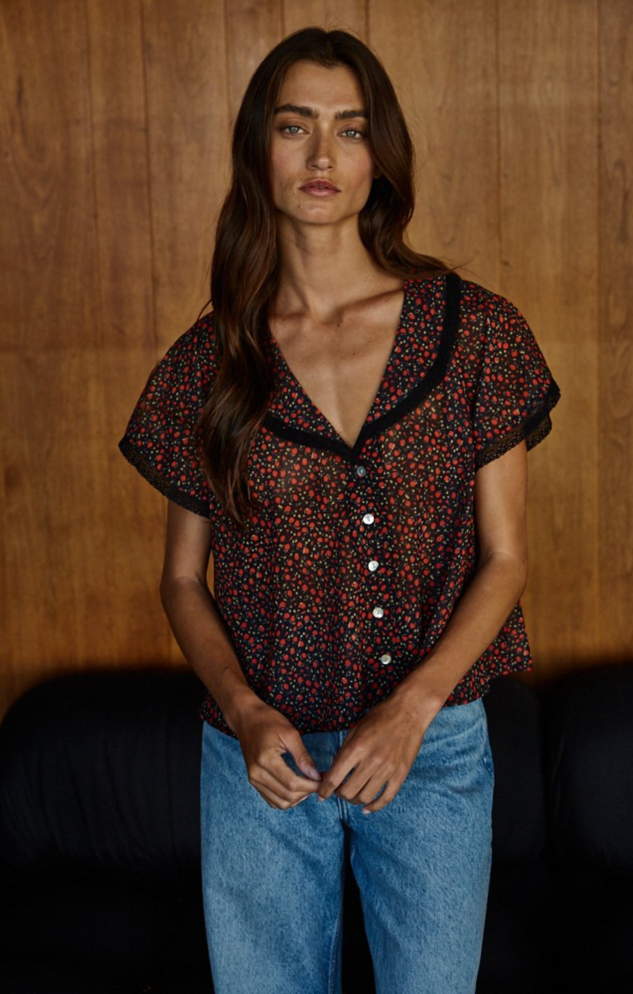 Woman wearing a patterned blouse and blue jeans against a wooden background