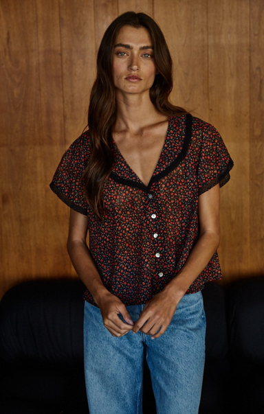 Woman wearing a patterned blouse and blue jeans against a wooden background
