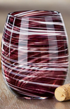 A stemless wine glass with a marbled pattern of deep burgundy and white swirls, shown on a wooden surface next to a cork.