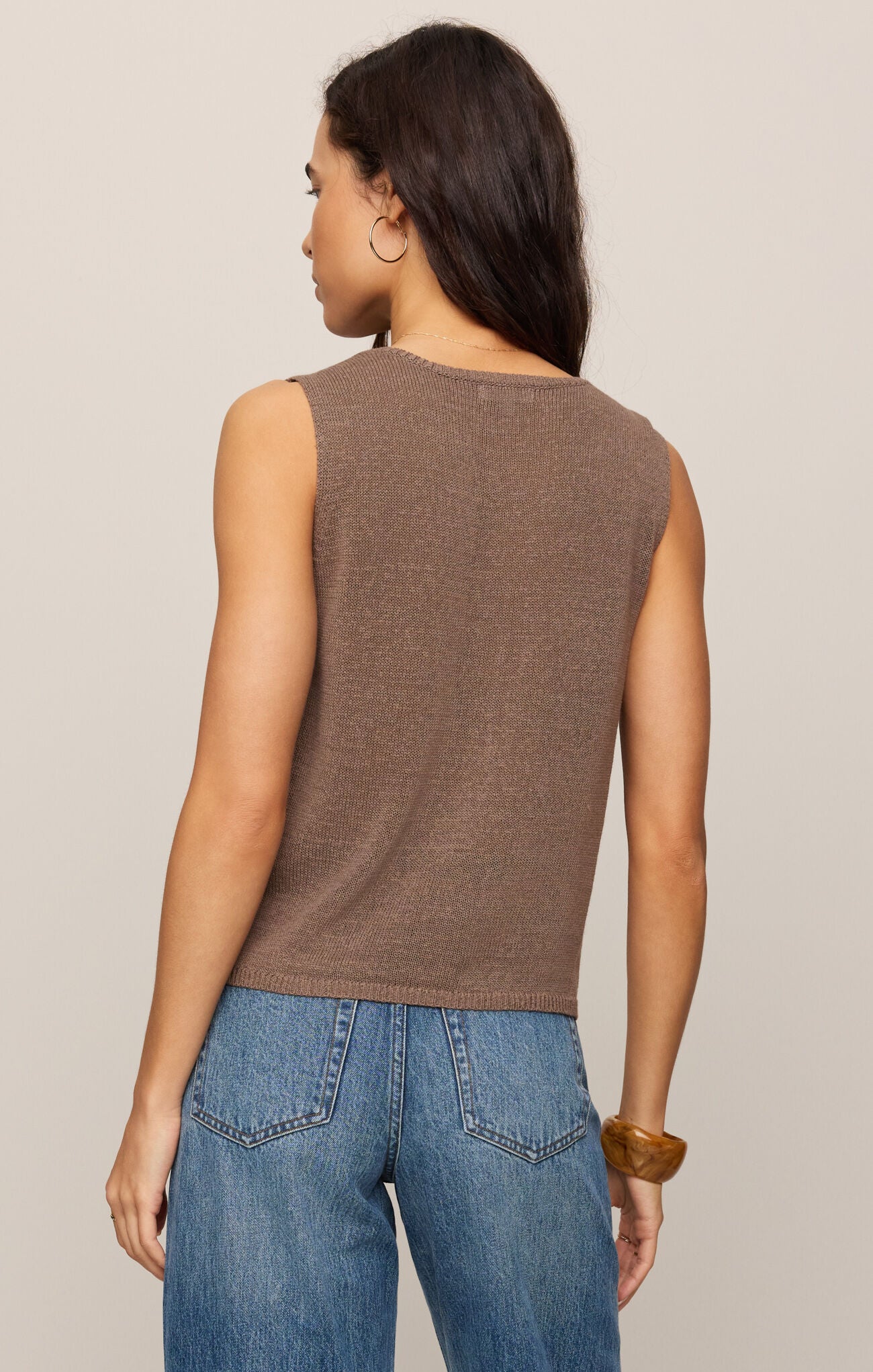 Woman wearing a brown sleeveless top and blue jeans against a beige background
