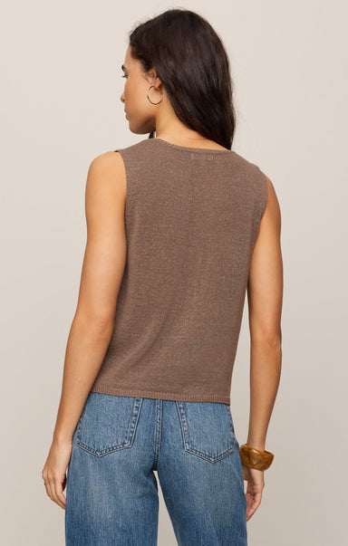Woman wearing a brown sleeveless top and blue jeans against a beige background
