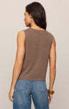 Woman wearing a brown sleeveless top and blue jeans against a beige background