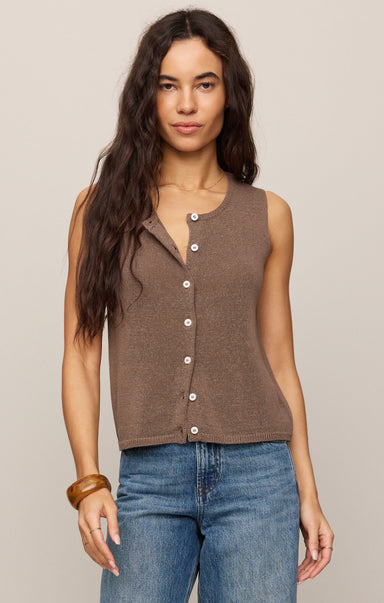 Woman wearing a brown sleeveless button-up top and blue jeans against a plain background