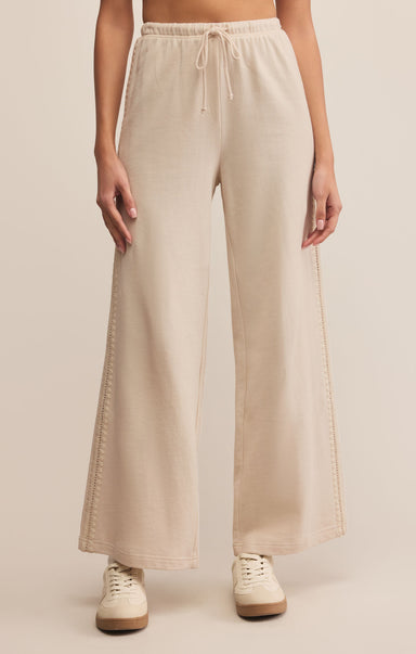 A pair of high-waisted, beige, straight-leg sweatpants with an elastic waistband and drawstrings. The pants are ankle-length and made of cotton.