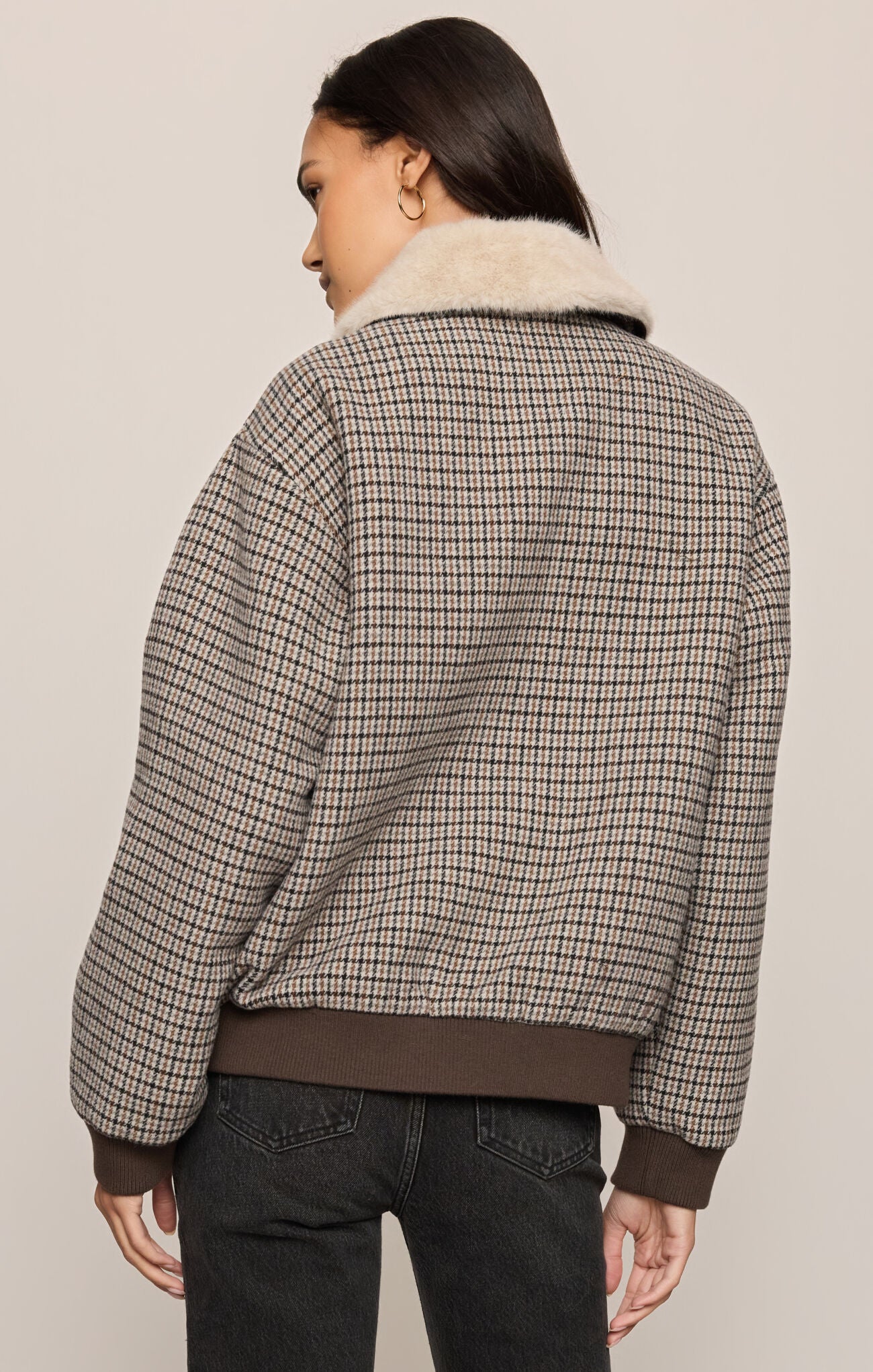 Person wearing a plaid jacket with a fur-lined collar on a plain background