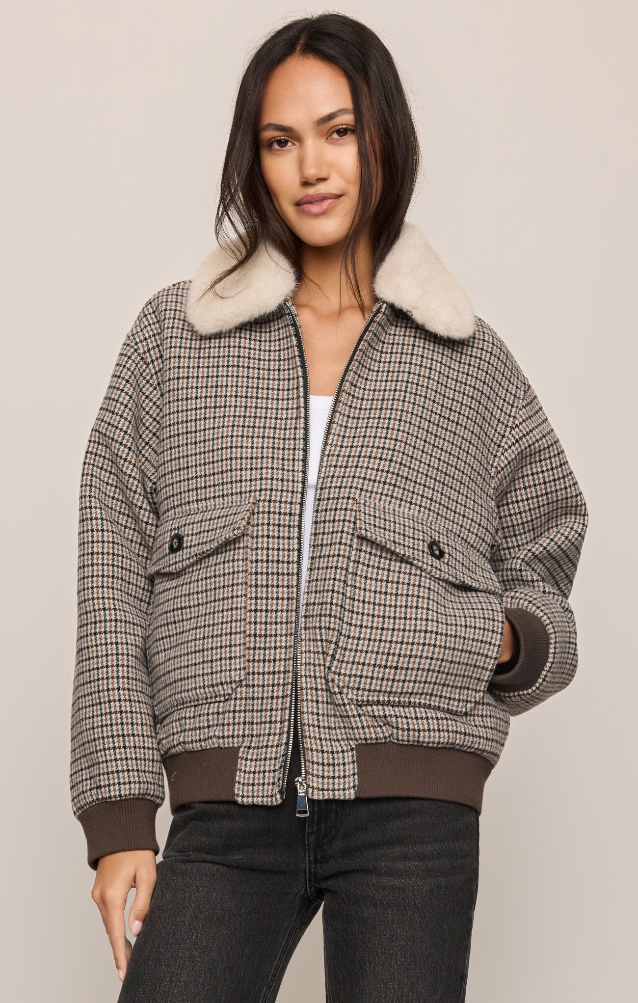Woman wearing a plaid jacket with a fur-lined hood on a beige background