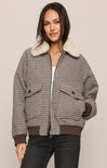 Woman wearing a plaid jacket with a fur-lined hood on a beige background