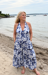 Woman in a blue floral dress standing on a beach with water and boats in the background