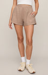 Person wearing beige shorts and white sneakers on a plain background