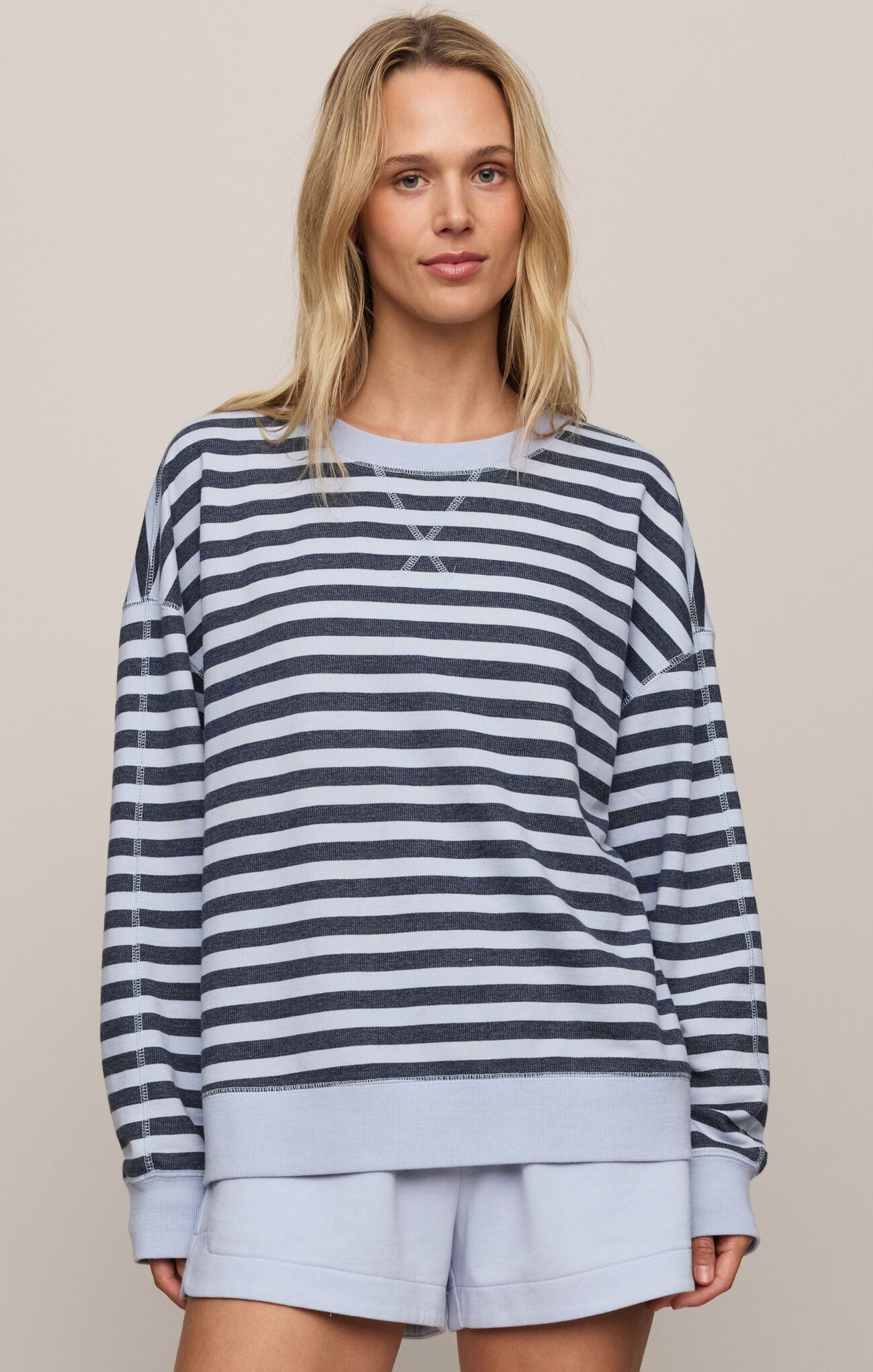 Woman wearing a striped sweater and light shorts against a neutral background