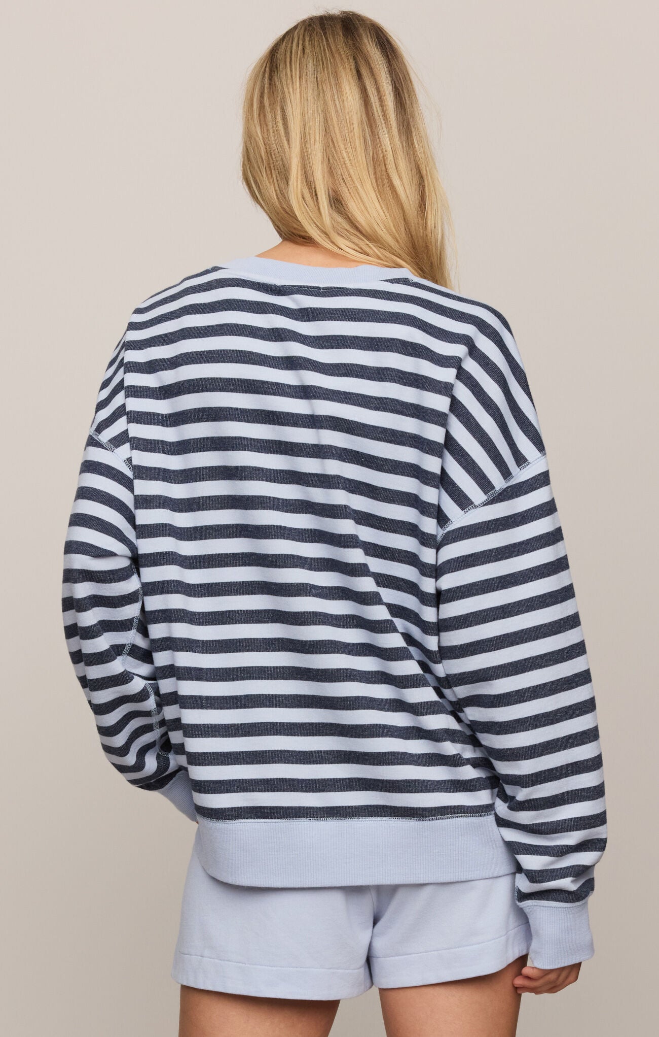 Person wearing a striped sweater and light blue shorts on a beige background