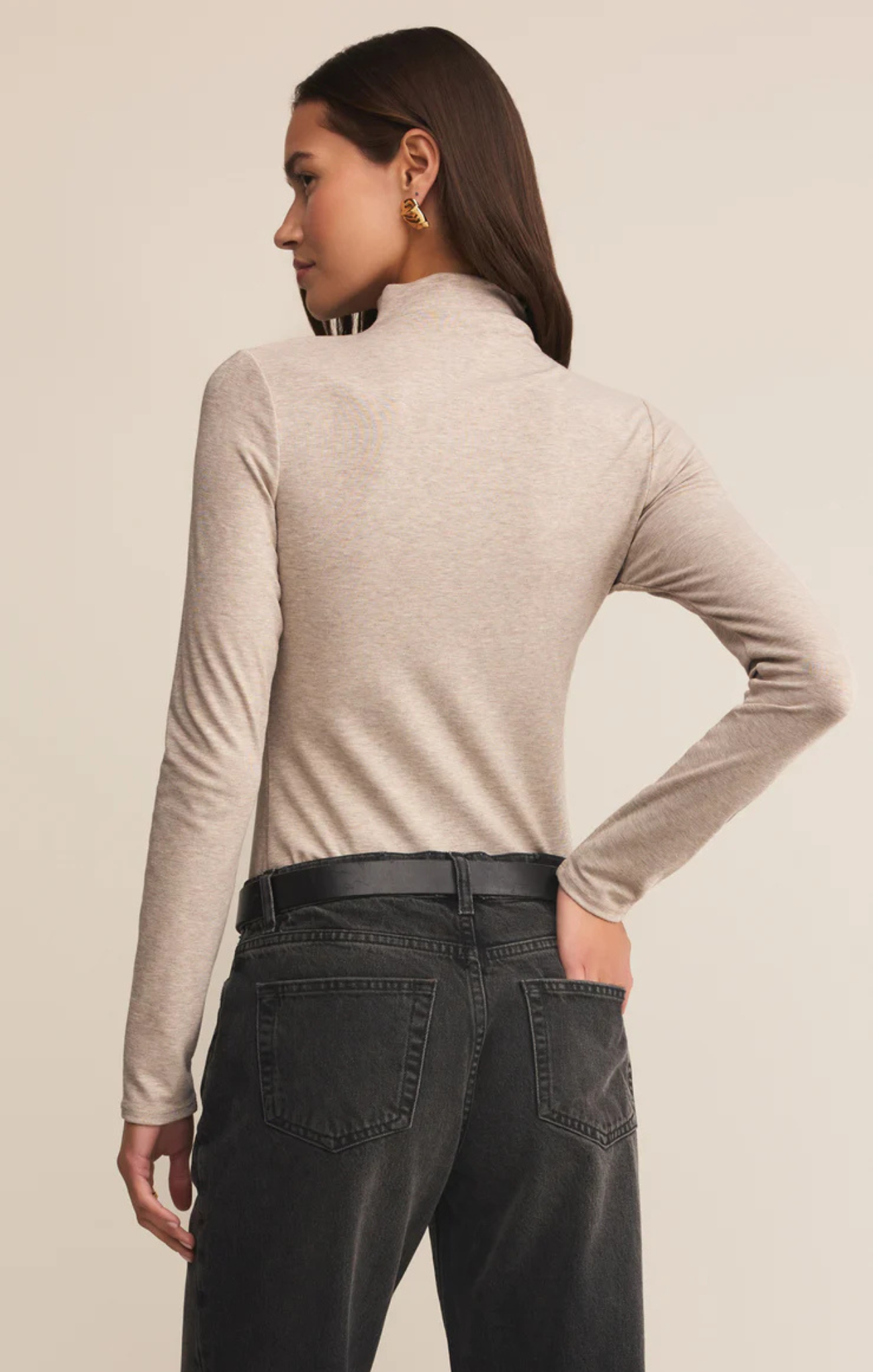 Woman wearing a beige long-sleeve top and black pants on a beige background