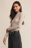 Woman wearing a beige turtleneck sweater and black jeans against a beige background