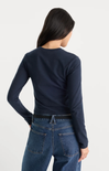 A woman shown from the back wearing a dark navy long-sleeve crewneck top and blue jeans against a plain light gray studio background.