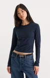 A woman modeling a dark navy blue long-sleeve crop top paired with blue jeans against a plain light gray studio background.
