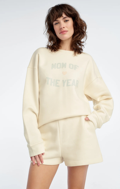 Woman wearing a cream-colored 'Mom of the Year' sweatshirt and shorts on a white background