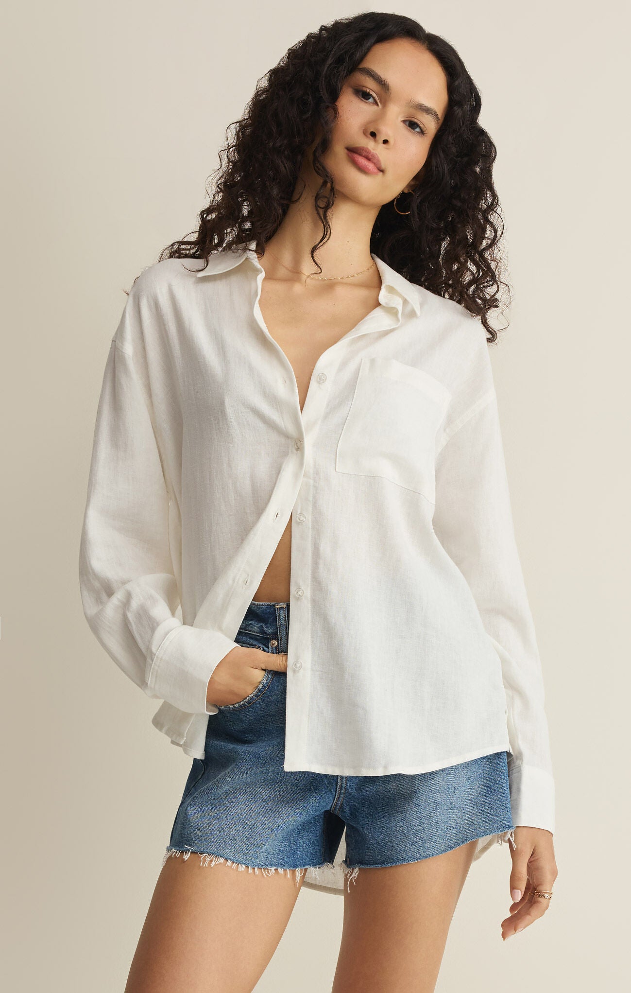 Woman wearing a white button-up shirt and denim shorts on a beige background